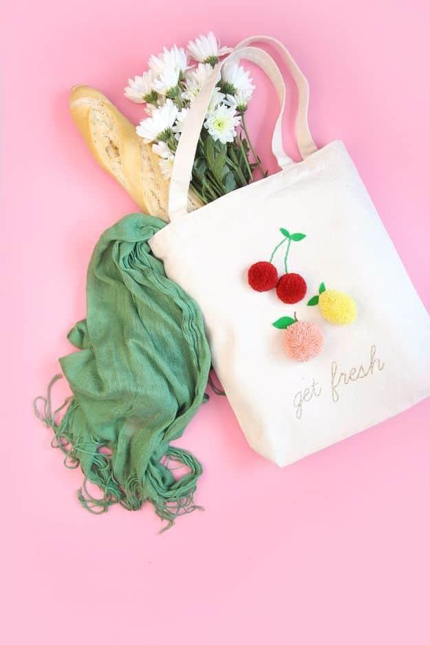 Canvas market tote with red, peach and yellow yarn pom pom fruit and gold stitched lettering on a pink background