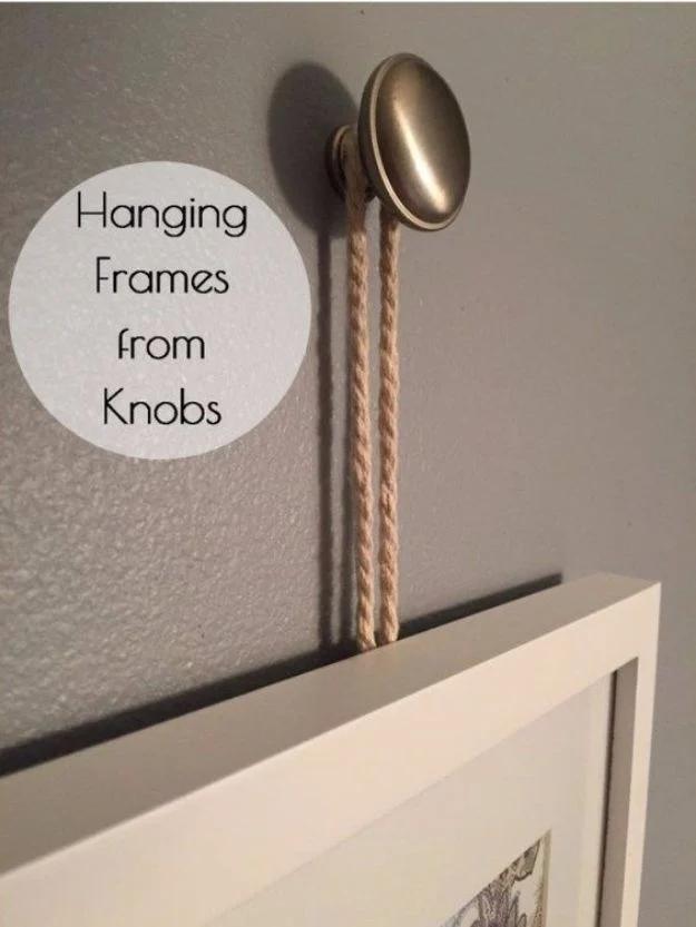 White picture frame hanging from a loop of pale cord rope over a brushed nickel drawer knob screwed into a grey wall