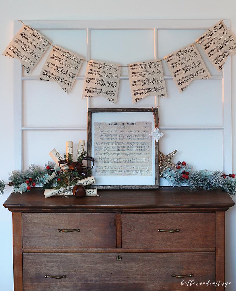 Basket of rolled vintage sheet music pages tied with twine and tucked with fresh pine sprigs and sleigh bells