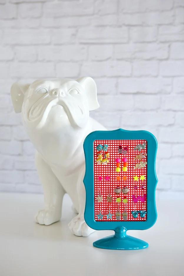 Pretty earrings holder, a teal plastic frame filled with plastic canvas and earrings beside a white bulldog statue