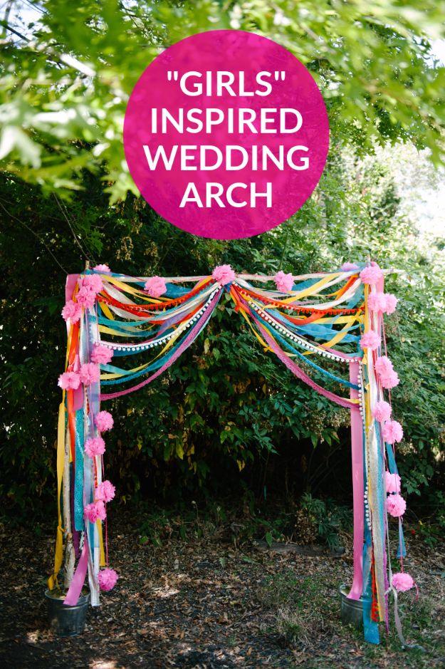 Outdoor wedding arch of birch poles draped with colorful ribbons and pom poms, with a typeset pink badge