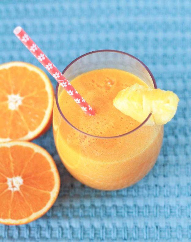 Tropical pineapple orange and mango juice with a pineapple wedge and a paper straw beside halved oranges