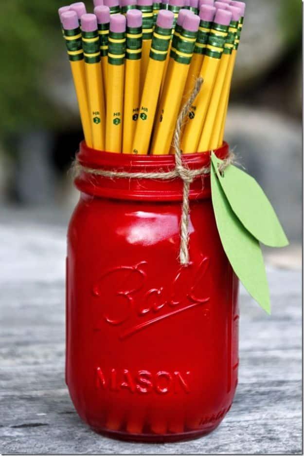 Bright red painted Ball mason jar tied with twine and two green paper leaves, filled with yellow pencils