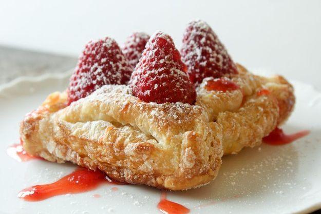 Fresh strawberry tart made from puff pastry topped with whole berries, powdered sugar and red berry sauce
