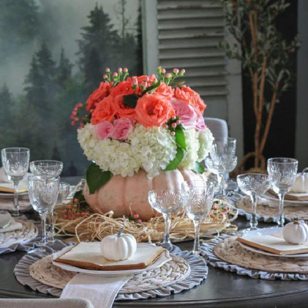 Pale pumpkin hollowed out and filled with coral roses and white hydrangeas as a centerpiece on a set dinner table
