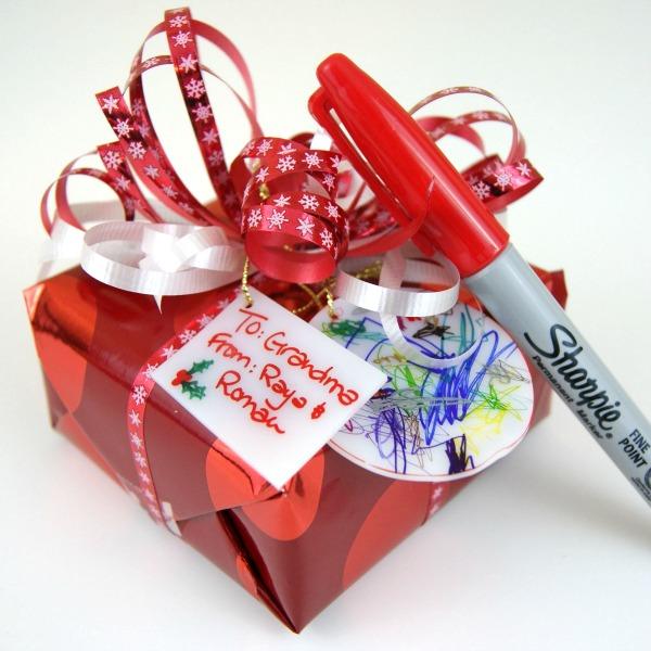 A red foil wrapped gift with a shrink plastic tag drawn on in marker, tied on beside a handwritten paper tag
