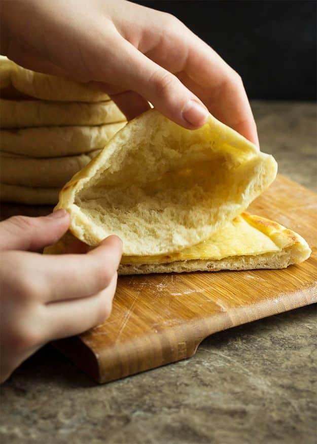 Homemade Greek pita bread puffed round and golden with one torn open to reveal the hollow pocket inside