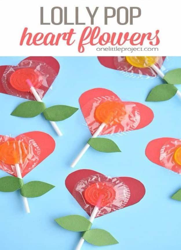 Five lollipops taped to red and pink paper hearts with green paper leaves rolled onto the sticks, on pale blue