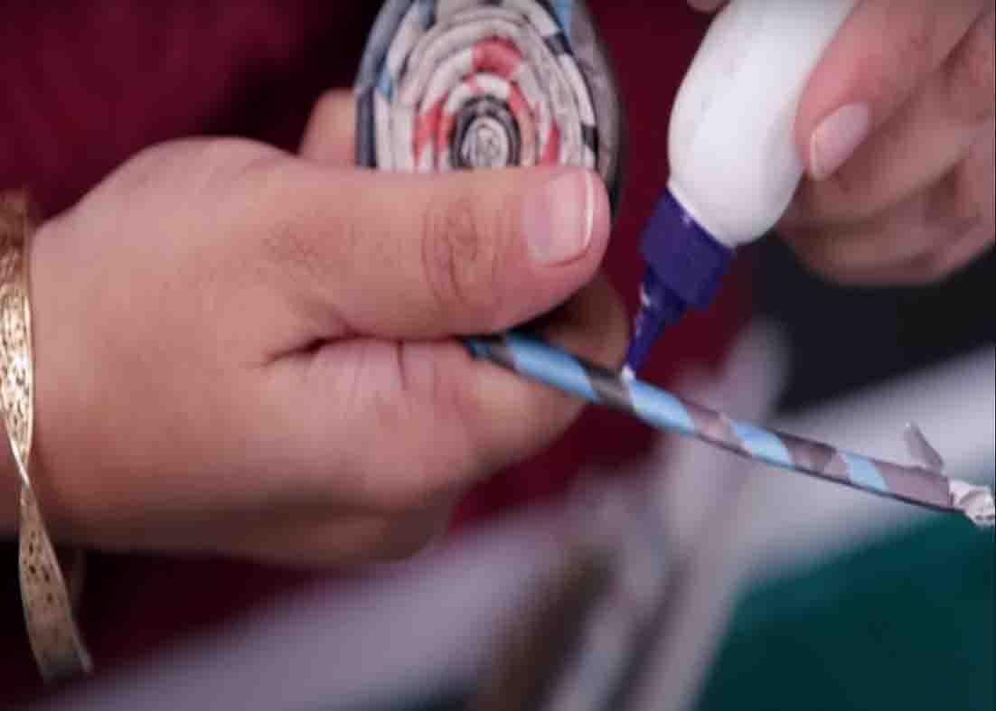 Gluing the ends of the rolled newspaper strip to secure it