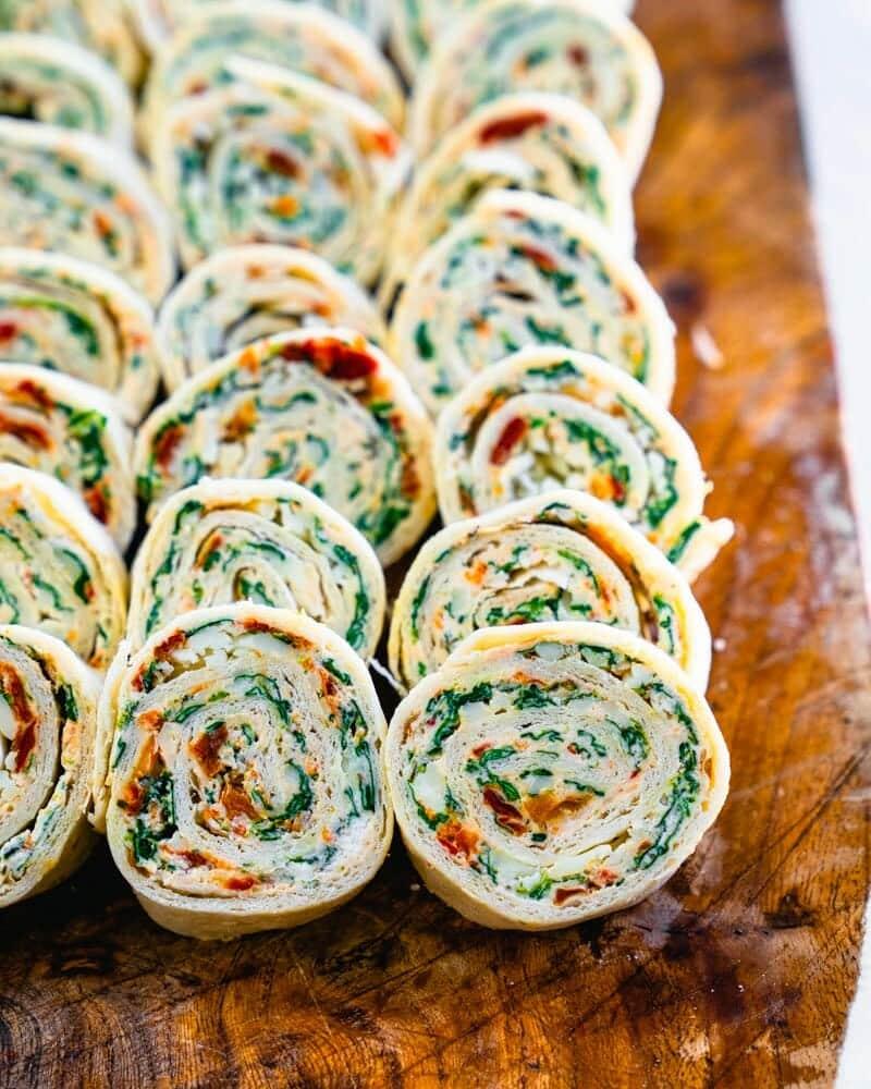 Tortilla pinwheel bites sliced into spirals showing spinach and red pepper cream cheese on a wood board