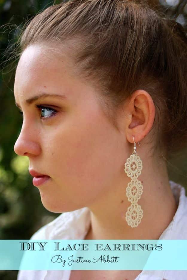 A pair of stiffened white lace earrings hanging from gold wires against a plain grey background so the pattern shows.