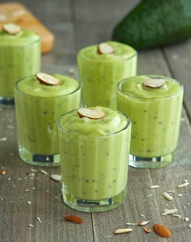 Vanilla and honey avocado pudding in four small glasses topped with sliced almonds on a dark wooden board