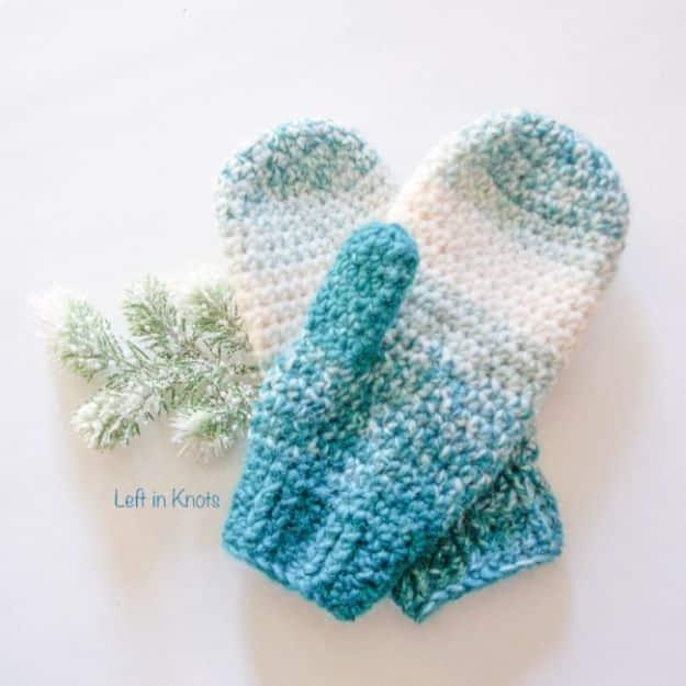 DIY clothes for winter, a pair of crochet mittens in white fading into teal, laid flat with a sprig of greenery