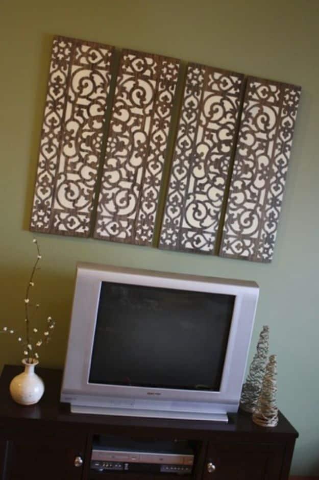 Four tall dark stained wood panels with an ivory scrollwork pattern sprayed through a doormat, above a television