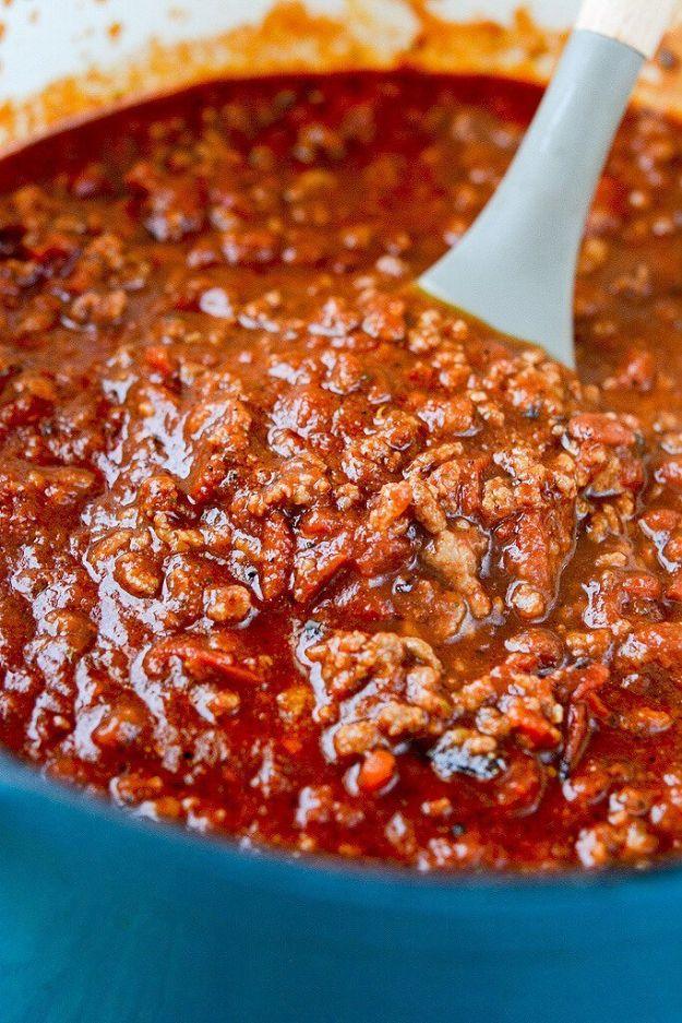 Slow cooker tailgate chili simmering in a teal pot with a white spoon resting in the thick red chili