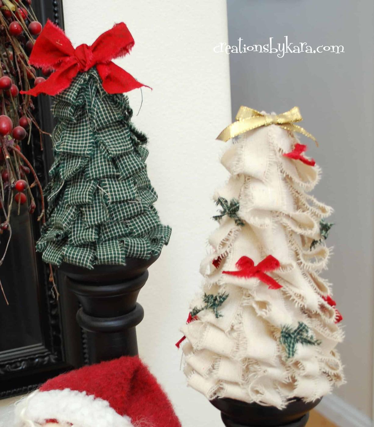 Two Christmas trees of ragged fabric strips, one green plaid and one cream, standing on black candlesticks with ribbon bows
