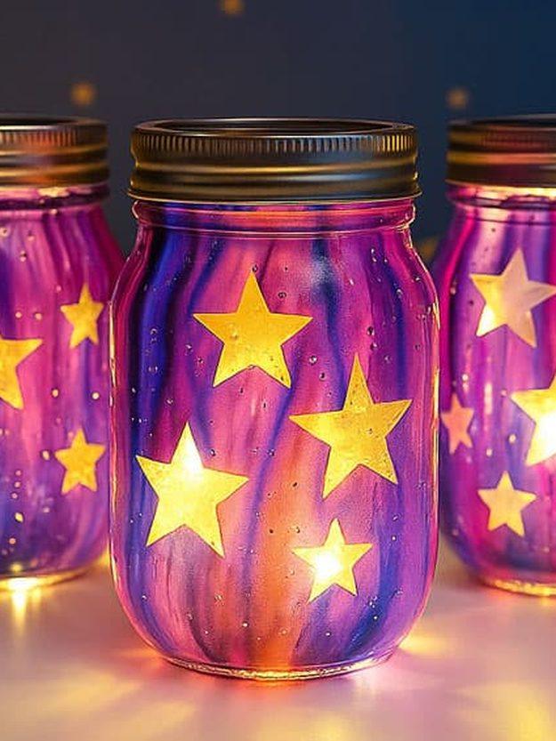Galaxy mason jars painted purple and pink with star shapes cut out and lit from inside by tea lights