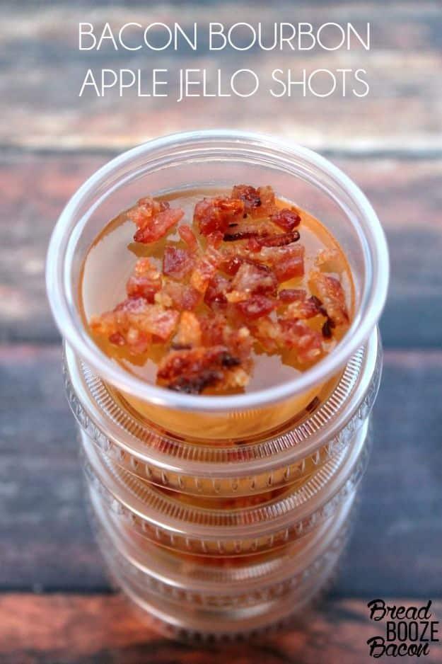 Bacon bourbon apple jello shots in two ounce plastic cups, each one topped with a piece of candied bacon