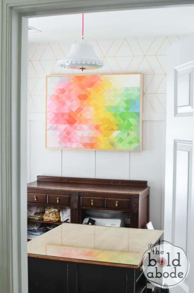 Large pixelated triangle canvas painting in rainbow colors hanging above a dark wood sideboard in a bright doorway