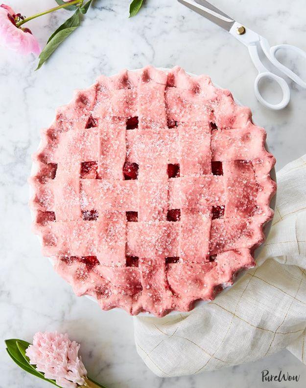 Strawberry pie with a pink lattice crust dusted in sanding sugar on marble beside scissors and a peony