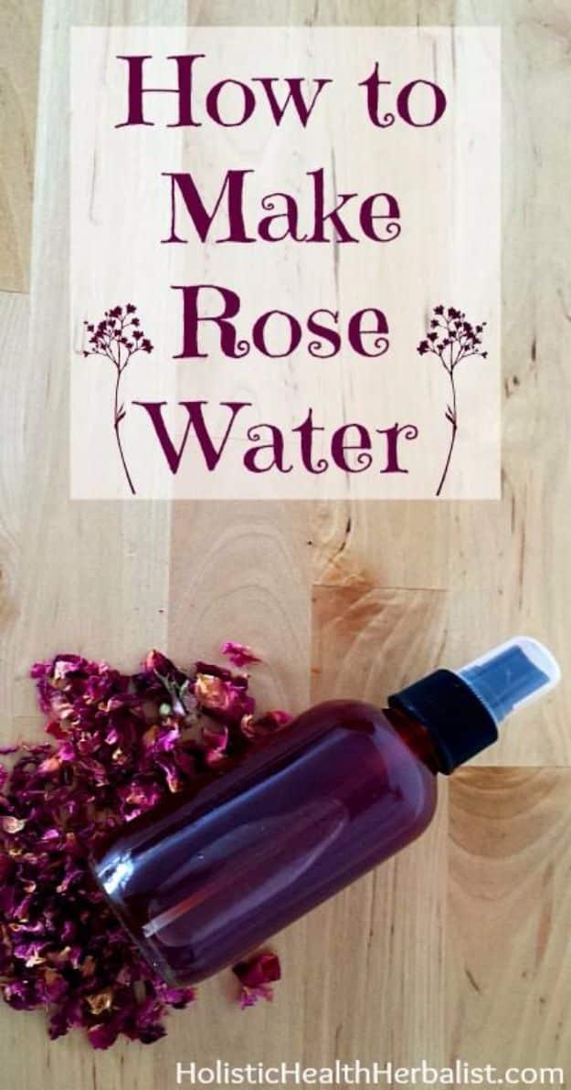 Rose water, a dark amber spray bottle lying on pale wood beside a heap of dried deep pink rose petals