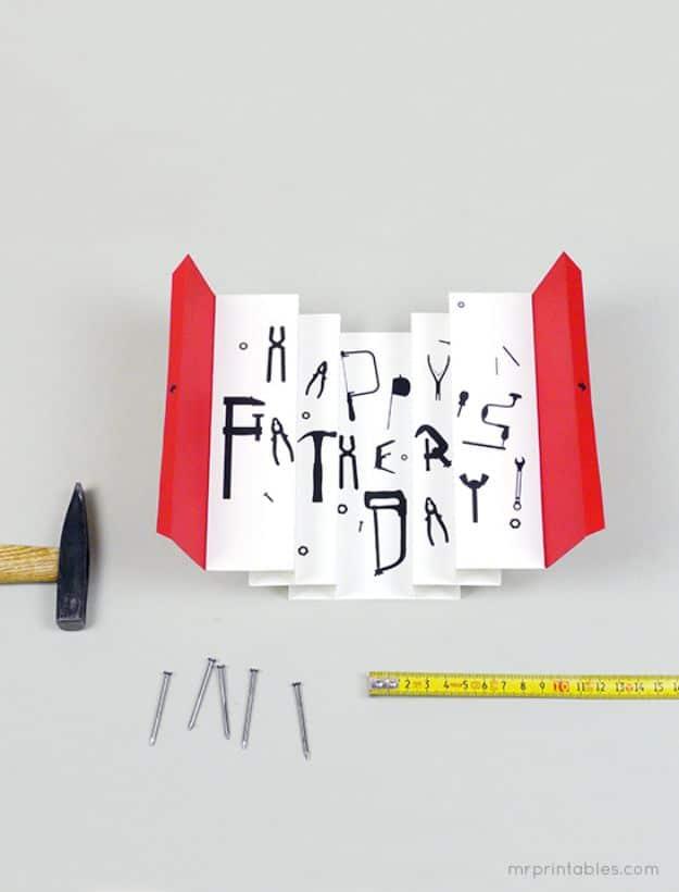 3D paper tool box card open on a gray desk, tools spelling Happy Father's Day, with a hammer, nails and a tape