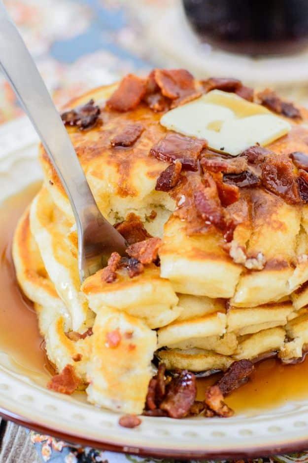 Maple bacon pancakes stacked with a pat of butter melting on top, chopped bacon and maple syrup poured over