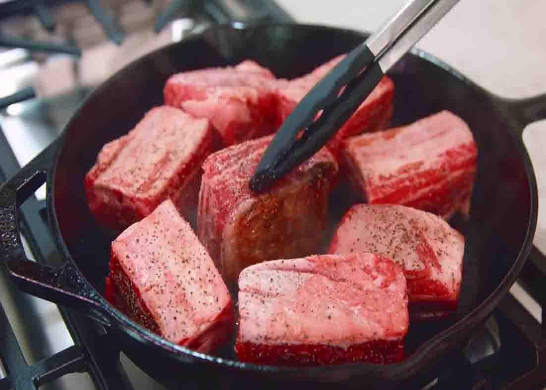 Searing the beef short ribs before placing them in the slow cooker