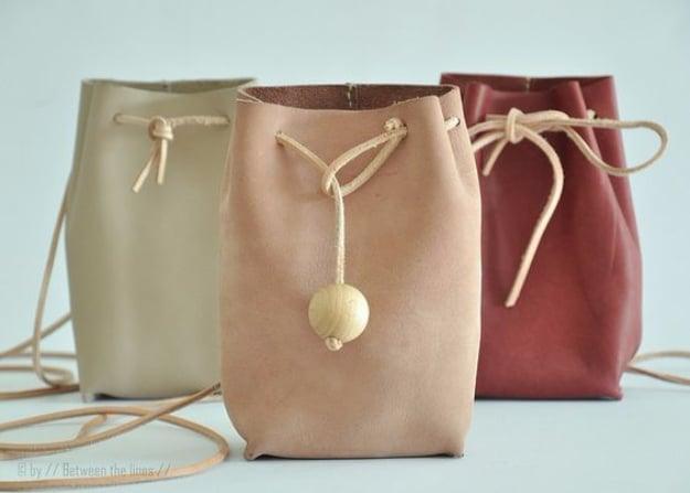 Three small leather drawstring pouches in sage, blush and deep red with fine cords and one wooden bead