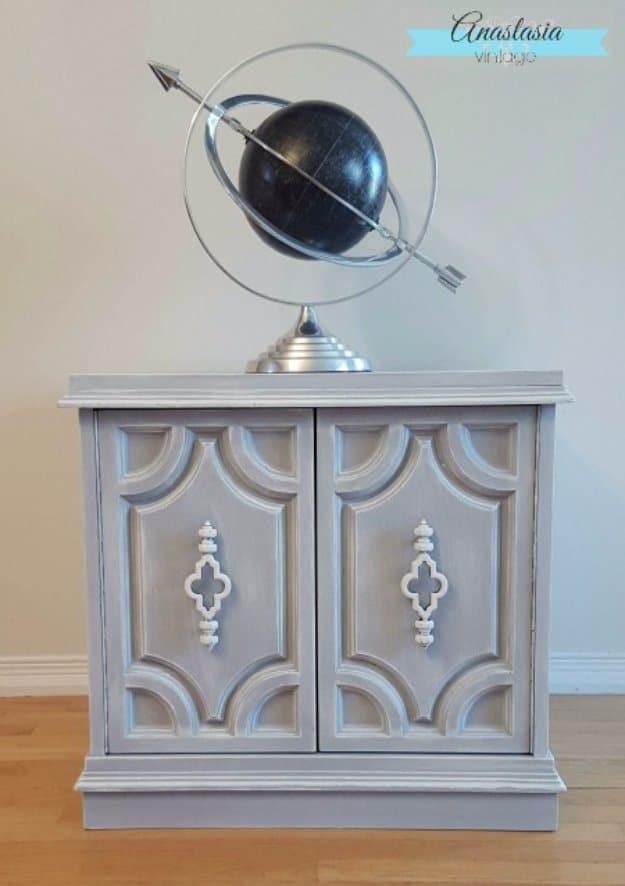 Weathered grey painted cabinet with raised molded panels and white hardware, styled with a brass armillary sphere