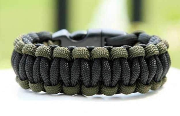 Black paracord survival bracelet edged along both sides in olive green cord, with a black release buckle
