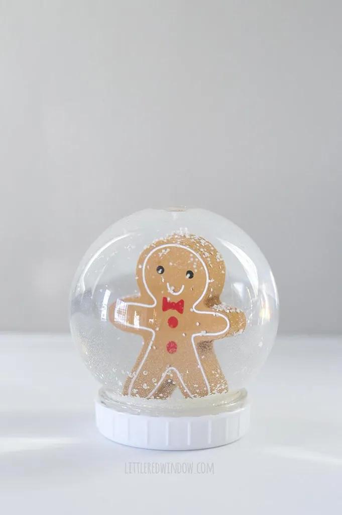Clear plastic snow globe on a white lid holding a smiling gingerbread man figure surrounded by drifting glitter