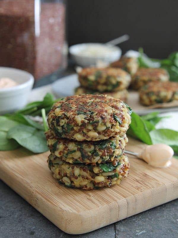 Stack of three pan fried spinach and cheddar quinoa cakes on a wooden board with fresh spinach leaves