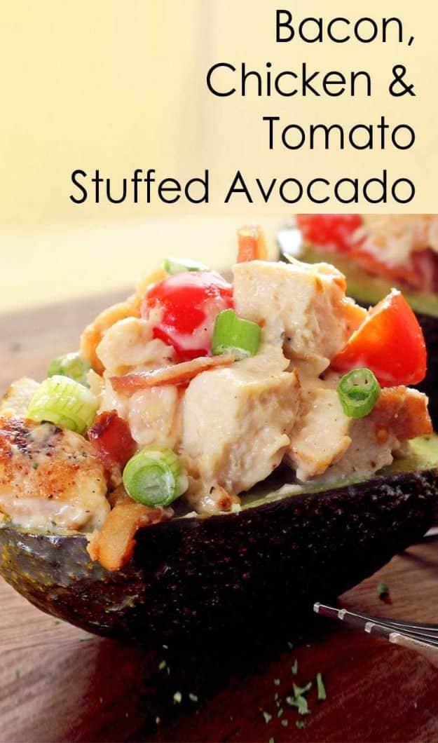 Bacon, chicken and tomato stuffed avocado halves on a wooden board beneath a large recipe title graphic