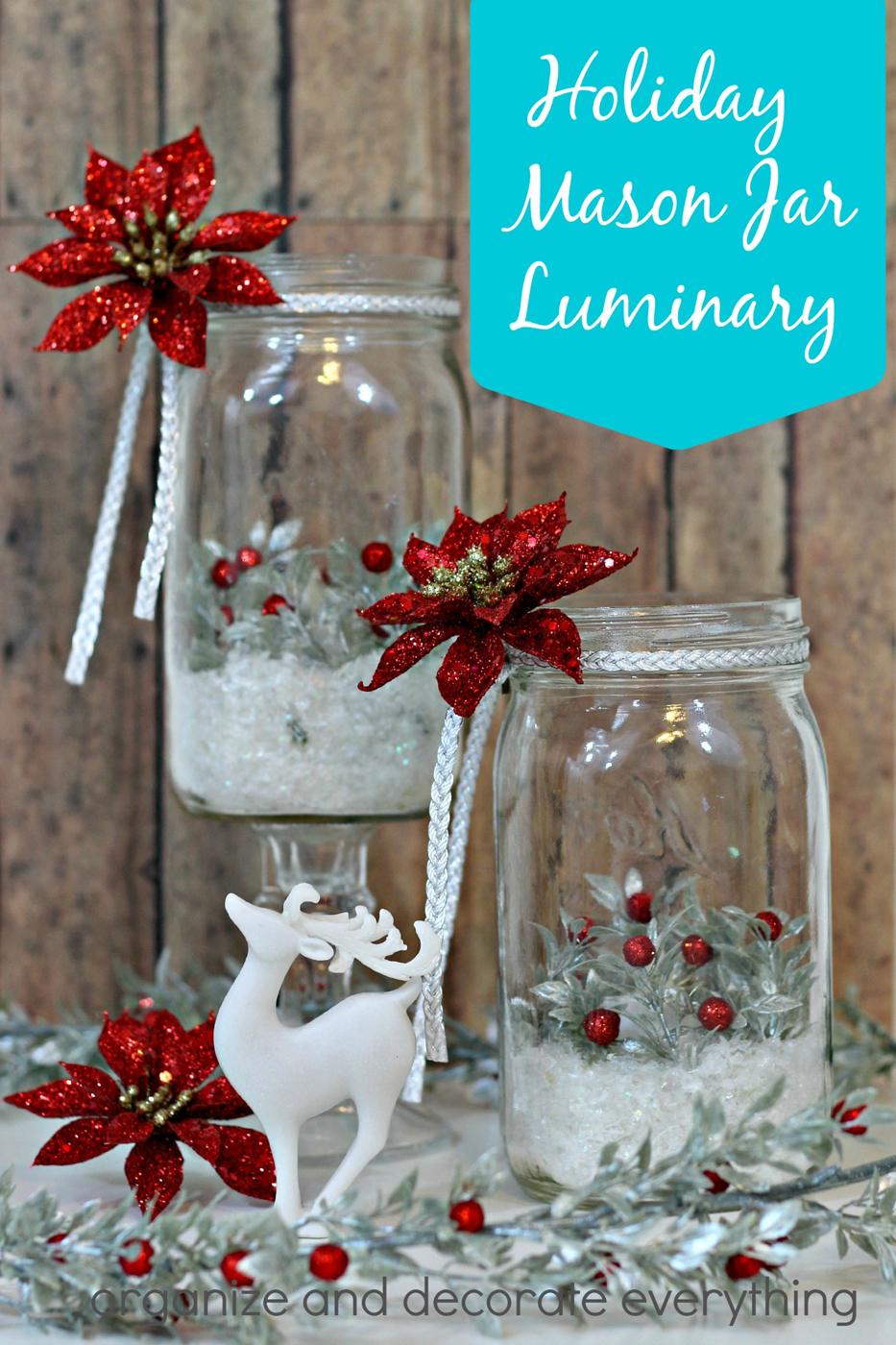 Two mason jar luminaries with faux snow, silver berry sprigs and red glitter poinsettias beside a white deer figurine
