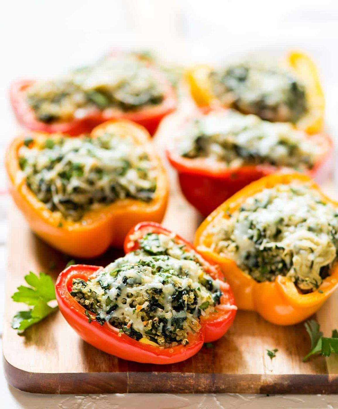 Red and yellow bell pepper halves stuffed with spinach artichoke quinoa filling and browned melted cheese