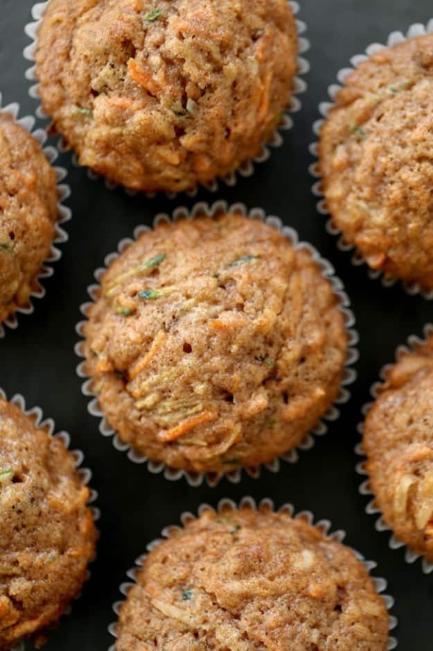 Morning glory muffins in white paper liners with flecks of carrot, zucchini and coconut across the tops