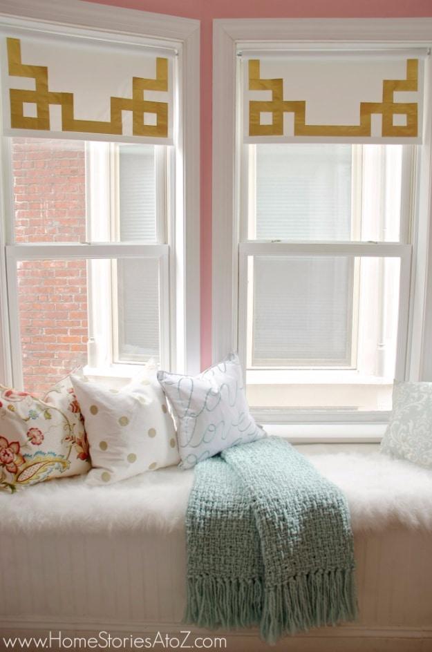 Two white roller shades in a window seat alcove, each bordered with a gold Greek key pattern made from duck tape