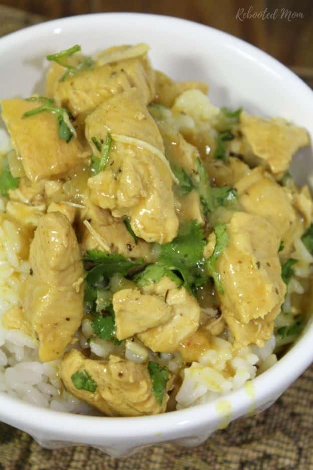 White bowl of golden basil chicken coconut curry with cilantro served over white rice on a pale surface