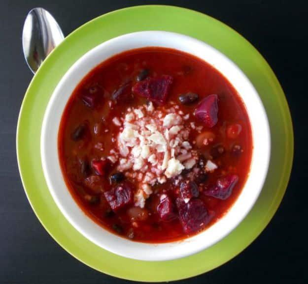 Bright magenta vegetarian beet chili in a white bowl on a green plate with crumbled white cotija cheese