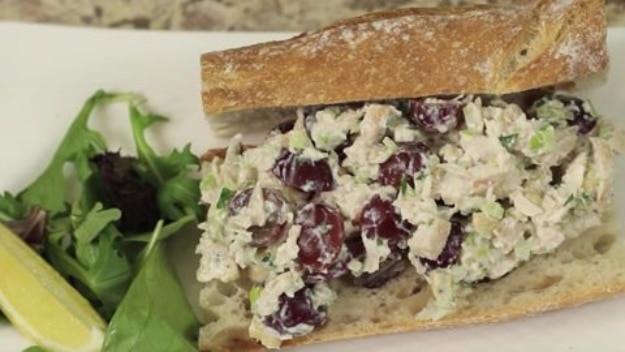 DIY chicken salad with dark grapes piled into a split ciabatta roll with mixed greens and a lime wedge