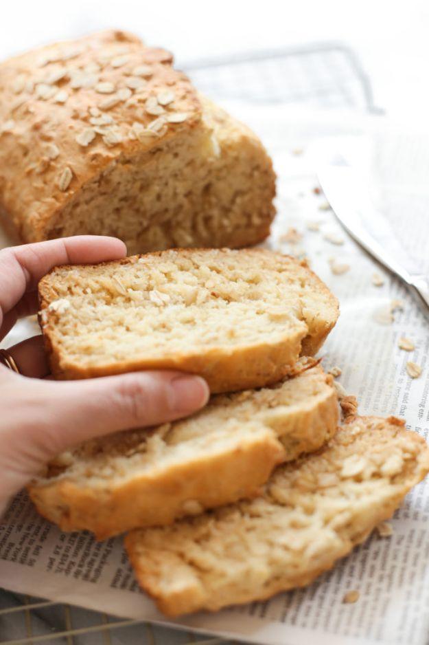 Gluten free honey oat bread sliced, a hand lifting one slice, with oats scattered over the golden crust
