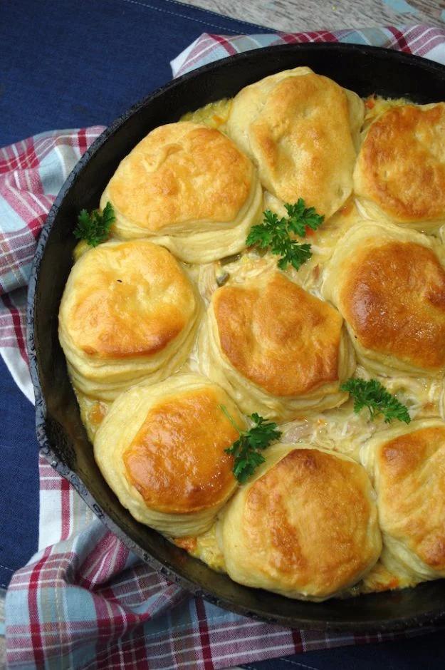 Cast iron skillet chicken pot pie topped with golden canned biscuits baking over creamy chicken filling