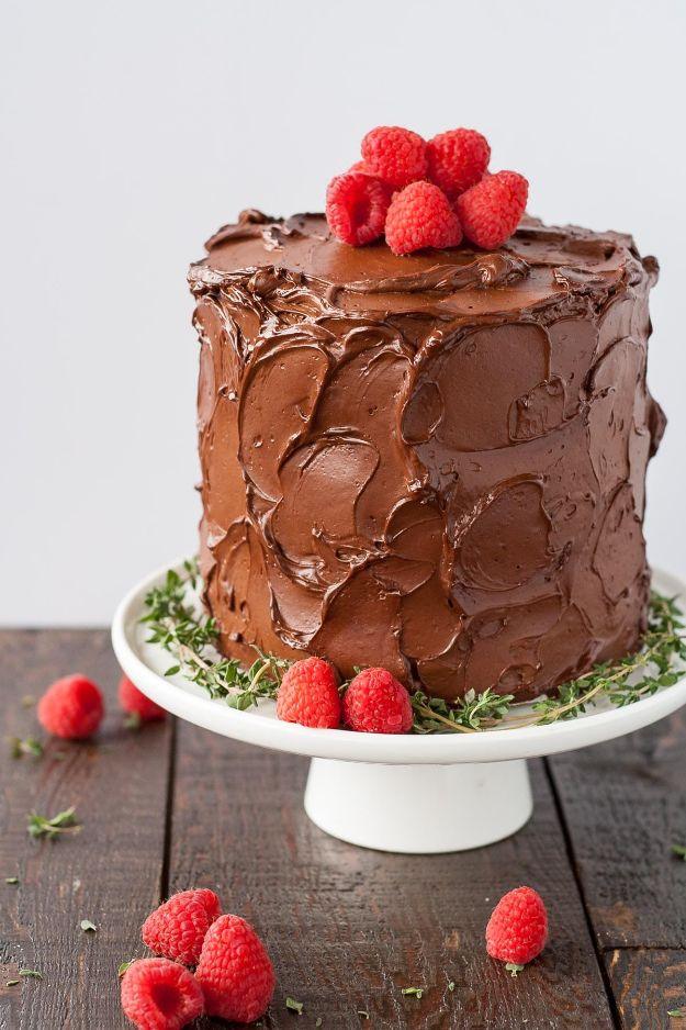 Chocolate raspberry layer cake with rustic dark frosting topped with fresh raspberries on a white cake stand