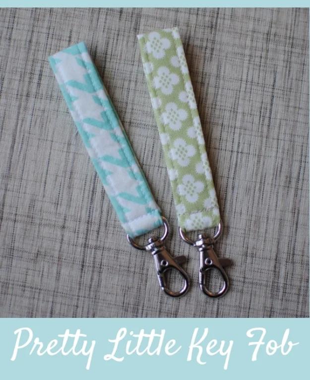 Two fabric key fobs in aqua chevron and green floral print, with silver lobster clasps, laid on gray linen