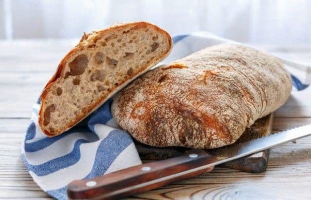Two crusty ciabatta loaves resting on a blue striped towel, one cut open to show the airy holey crumb inside