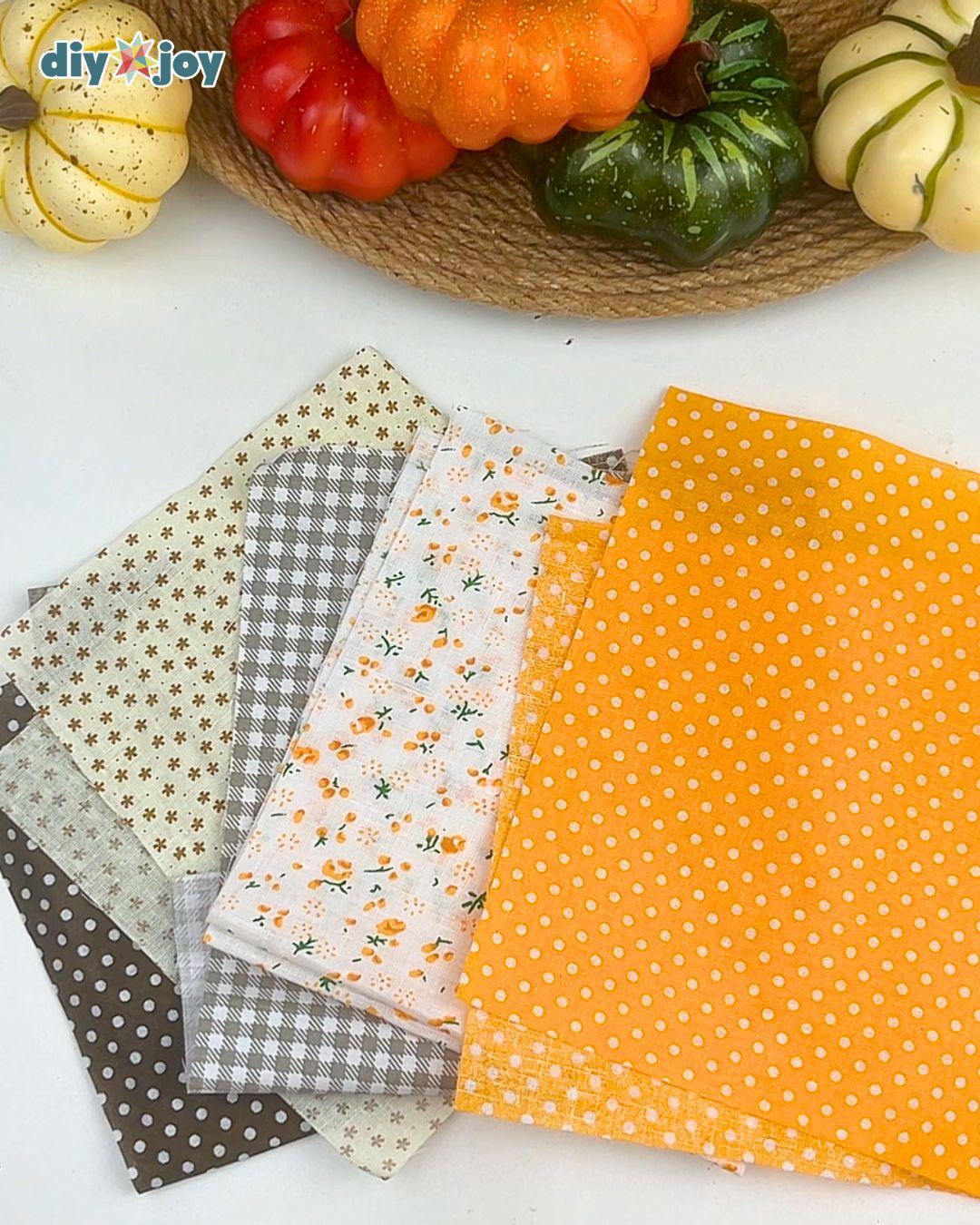 Fabric Scrap Crafts - four folded fabric squares in cream floral, gray gingham and mustard fanned out beside pumpkins