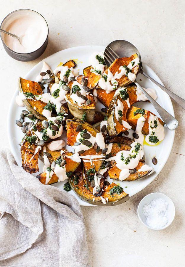 White platter of roasted pumpkin wedges drizzled with yogurt and green coriander sauce, seeds on top