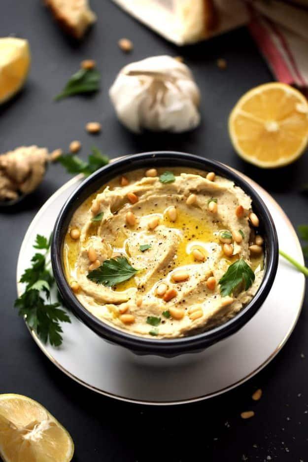 Creamy artichoke leek and white bean hummus in a bowl with olive oil and pine nuts, a gluten free party dip