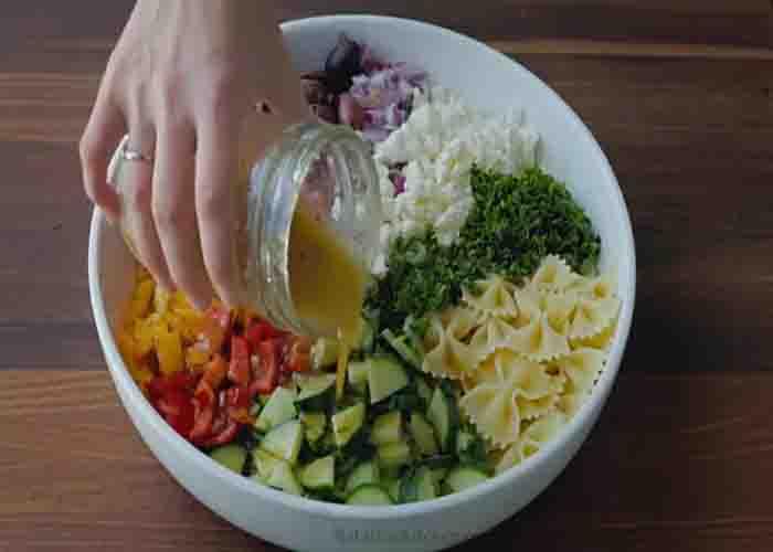 Drizzling the dressing over the Greek pasta salad